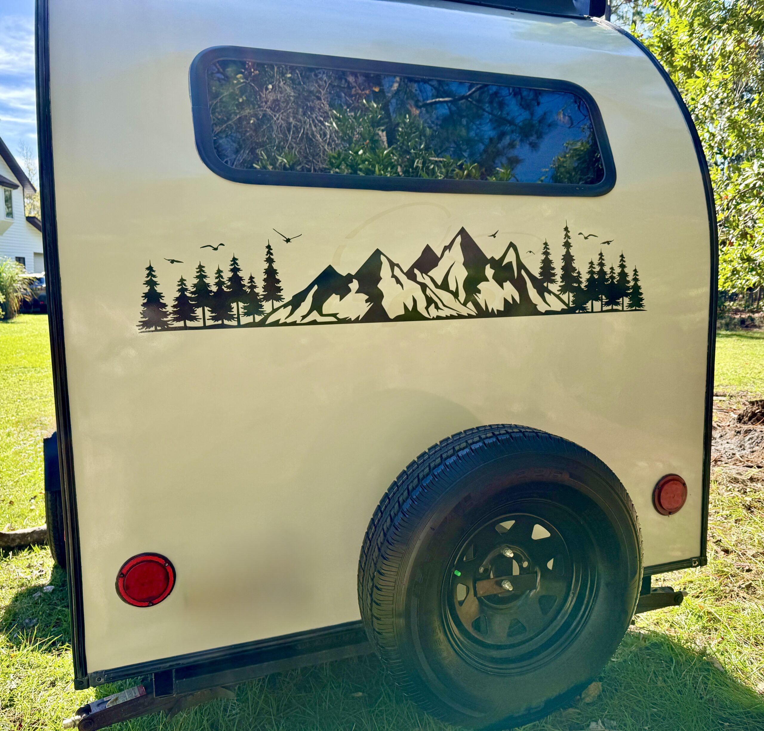 Close-up of the side of a 2019 Forest River R-Pod camper featuring a mountain and tree decal, alongside a black tire and red tail light.