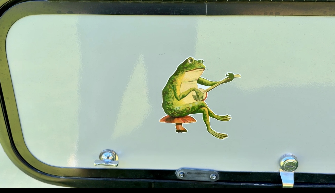 A colorful sticker of a frog playing a banjo while sitting on a mushroom, displayed on the exterior of a camper.
