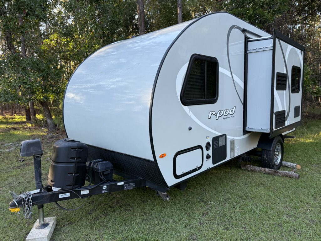 A 2019 Forest River R-Pod camper parked on grass, featuring a sleek, aerodynamic design with a slide-out section and RV hooking equipment.